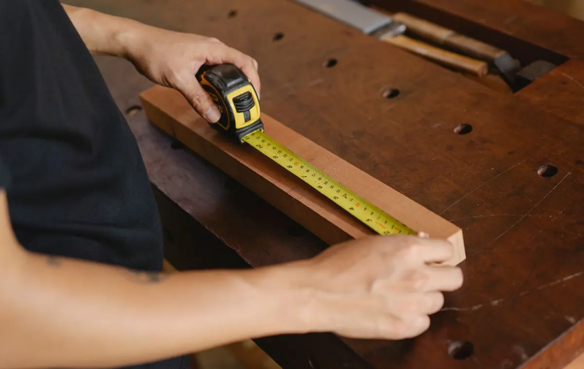 Artisan mesurant une planche de bois avec un mètre ruban